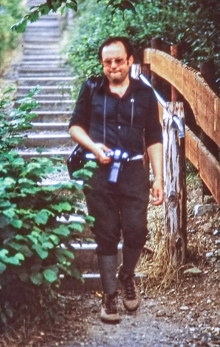 Mann mit Brille kommt eine Treppe herunter, in der Hand die Leica R3 mit dem langen APO-Telyt