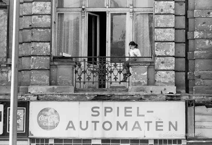 Mädchen auf dem Balkon eines Altbaus über dem Schild eines Spielautomaten-Salons