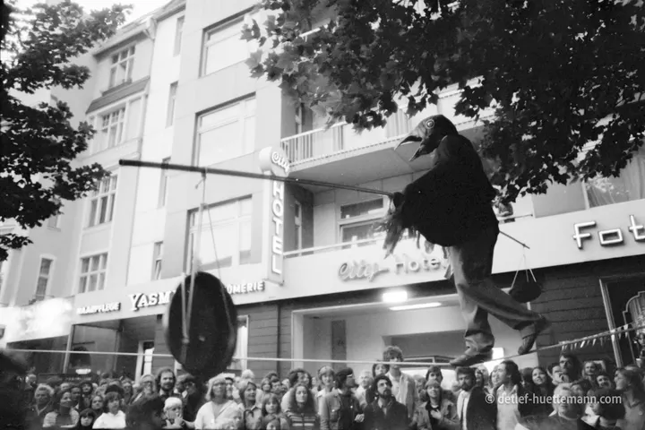 Seiltänzer im Vogelkostüm balanciert über dem Publikum, dahinter das city-Hotel