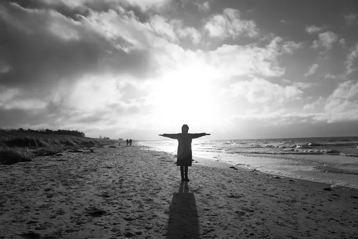 Mit ausgebreiteten Armen im Wind am winterlichen Ostseestrand