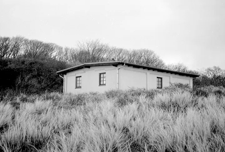 Haus im Dünengras unter dem bewaldeten Hochufer, fotografiert auf Ilford FP4