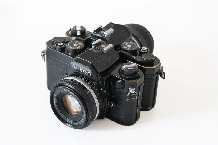 Zwei schwarze Nikon FM schräg von oben, an den Kanten schimmert Messing durch; vorne mit dem Nikon Series E 50 mm f/1,8