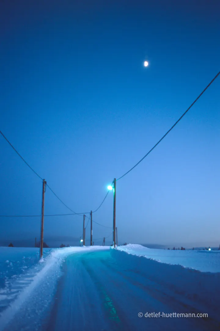 Dorfstraße in der blauen Stunde mit Mond und Telegrafenmasten