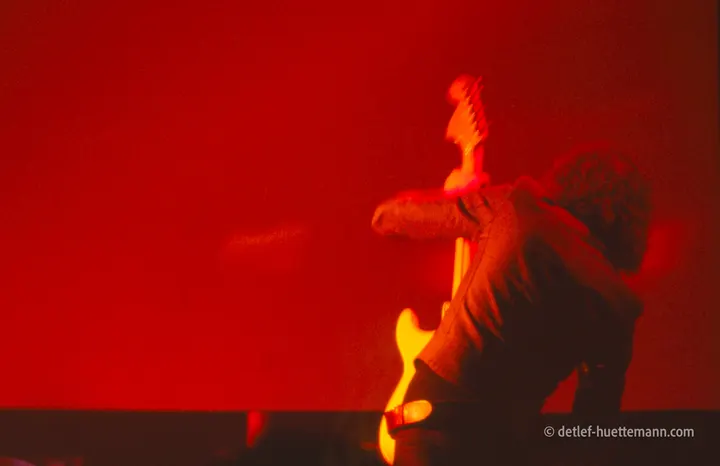 Ein Gitarrist von hinten, die Gitarre aufgestellt, vor roter Bühnenwand