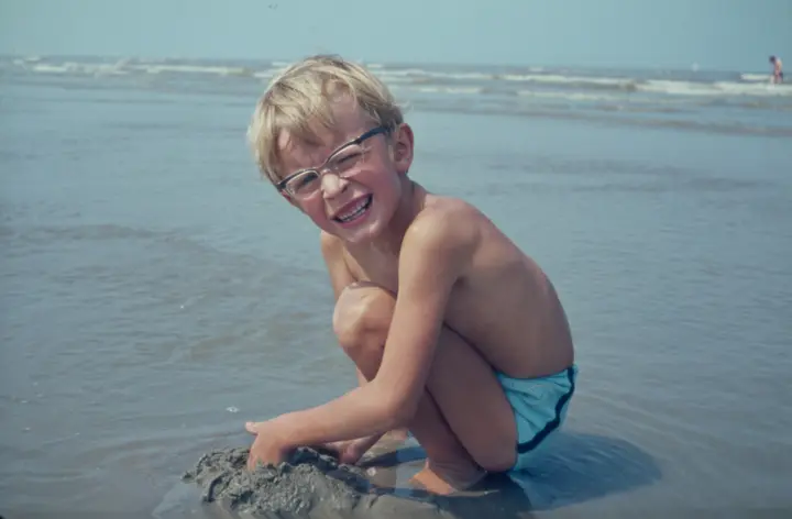 Junge mit Brille hockt lachend im flachen Wasser am Strand, Dia von 1971