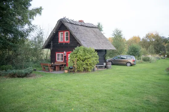 Reetgedeckte Holzhütte mit roten Fensterrahmen auf einer Wiese