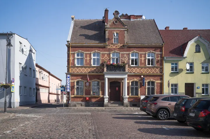 Backsteinhaus mit Säulenportal an einem gepflasterten Platz in Maszewo