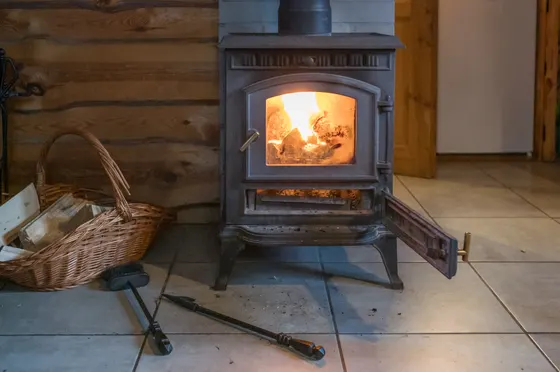 Gusseiserner Holzofen mit brennendem Feuer und Holzkorb