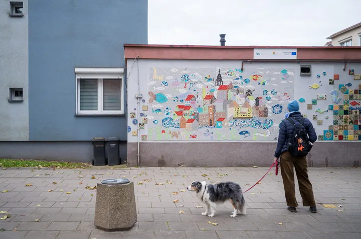 Frau mit Hund vor einem Wandmosaik mit Stadtansicht