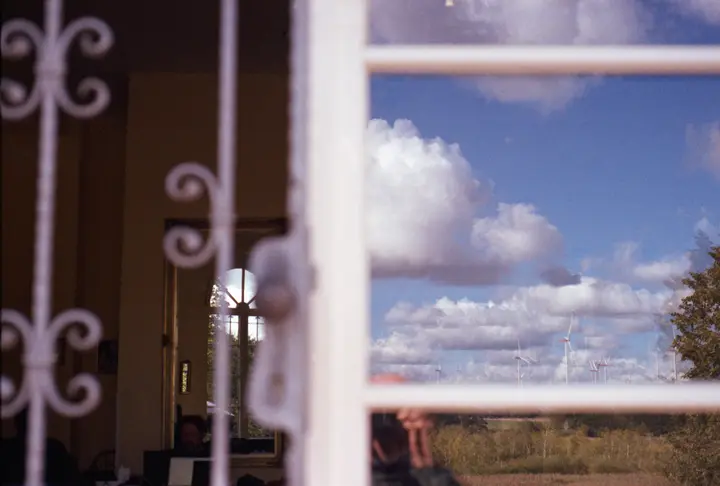 Blick durch ein Fenster: In der Scheibe spiegeln sich Wolken und Windräder, dahinter ein Innenraum