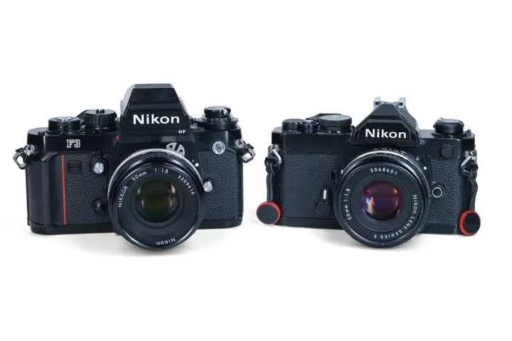Nikon F3HP und Nikon FM nebeneinander von vorn, beide mit 50-mm-f/1,8-Objektiv; die F3HP ist sichtbar höher und breiter